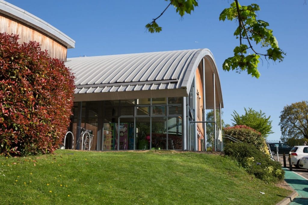 Building with glass walls and a curved grey roof on a small grassy hill